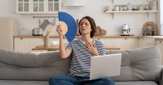Homeowner fanning herself next to an air conditioner blowing warm air